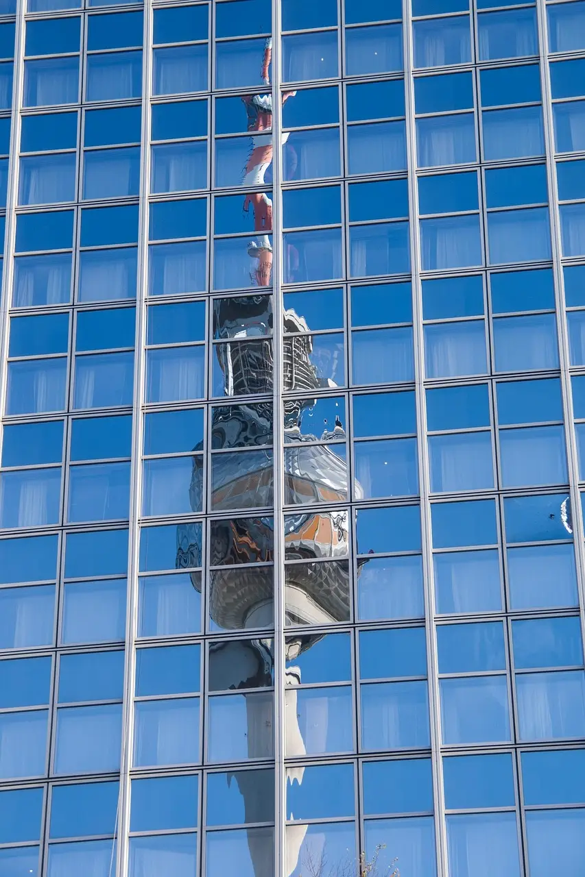 In einer Fassade aus Glasfenstern spiegelt sich der Berliner Fernsehturm als Symbol für die Menge an sanierungsbedürftigen Fenstern in Deutschland
